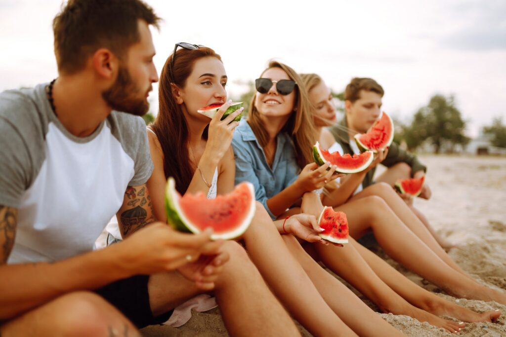 Young friends relaxing on the beach and eating watermelon. People, summer lifestyle