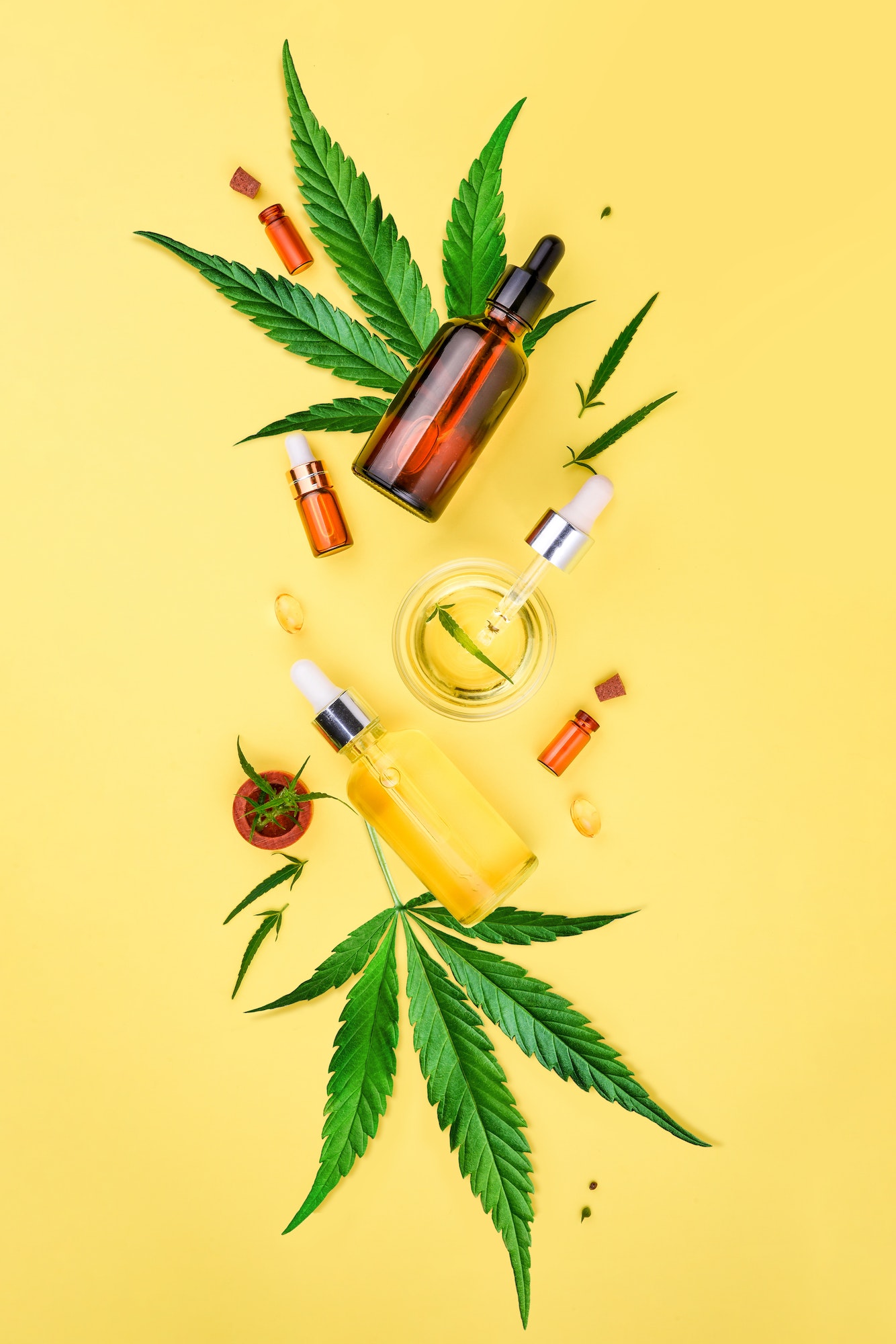 Glass bottles with CBD oil, THC tincture and hemp leaves on yellow background Cosmetics CBD hemp oil