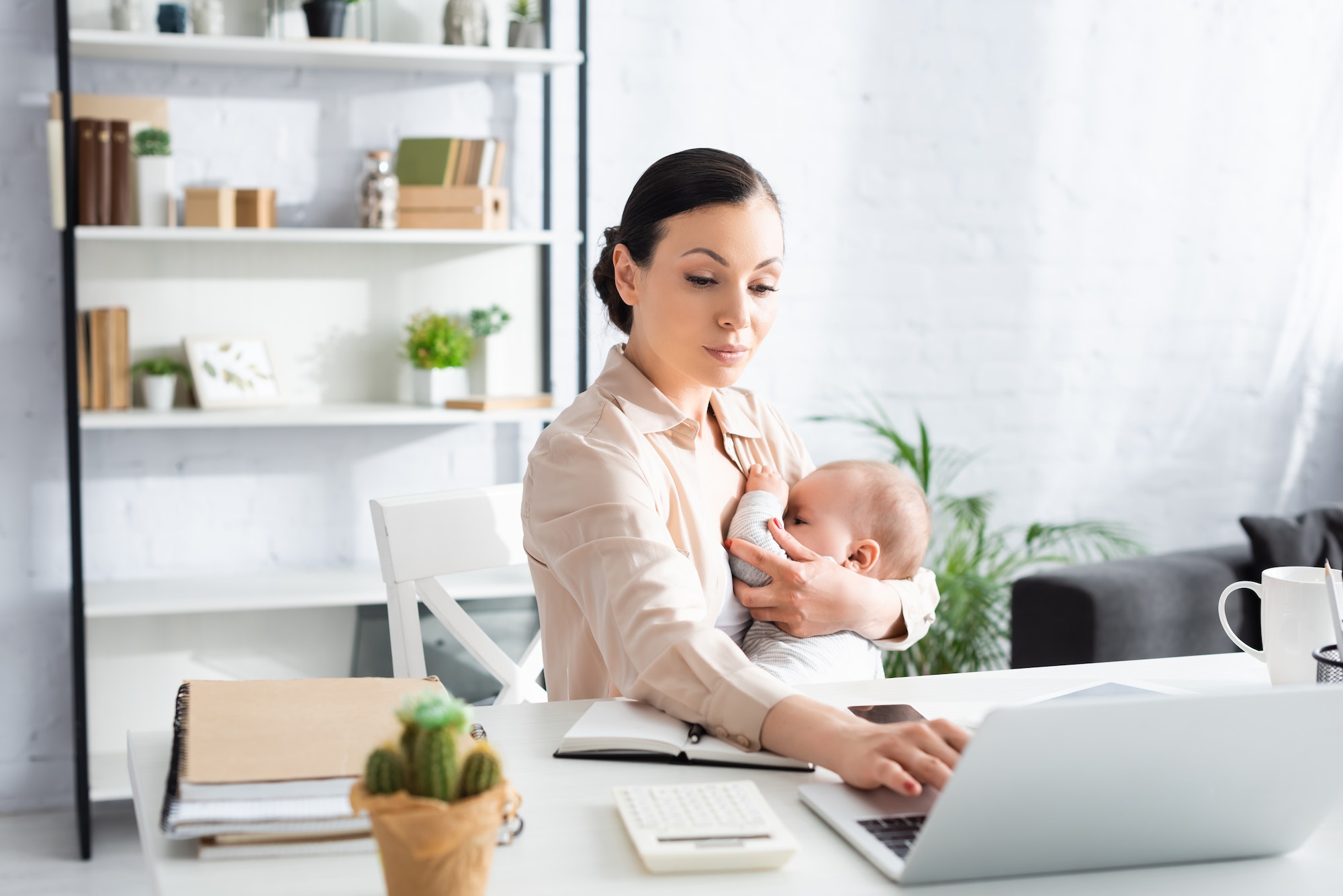 selective focus of mother breastfeeding infant son while using laptop at home