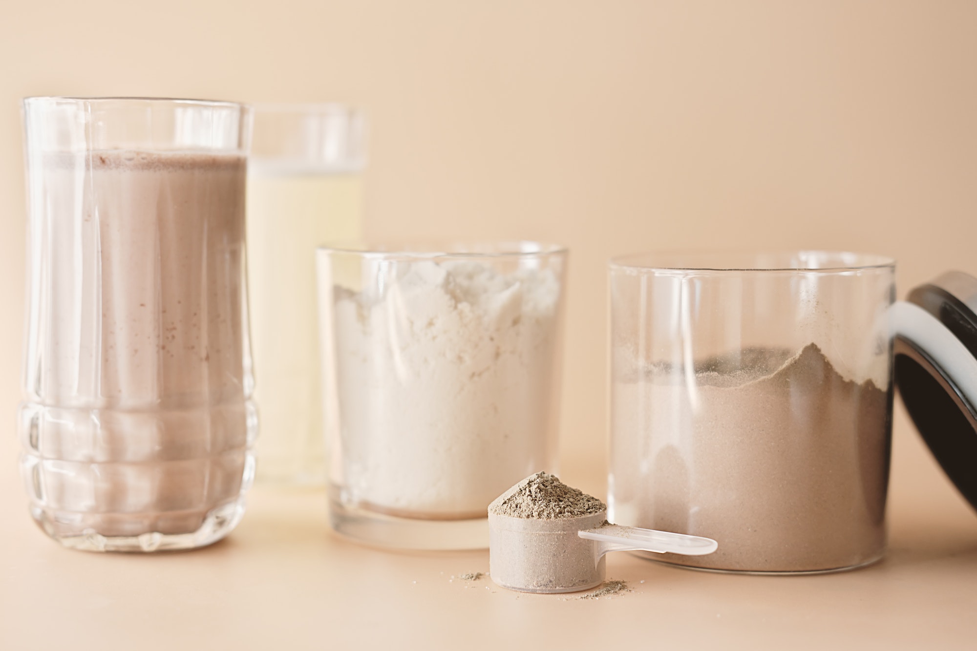 whey protein drink in a glass and jars with protein powder on beige background