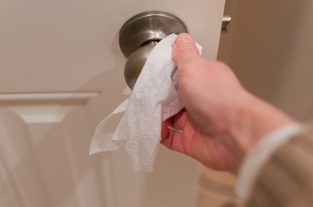 Hand wiping a door handle with an antiseptic Clorox wipe to remove germs